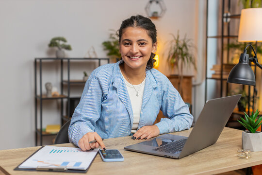 Indian freelancer accountant working with financial graph documents, calculate taxes for charts and reports at home office desk. Woman girl working on laptop, phone planning expenses budget. Lifestyle