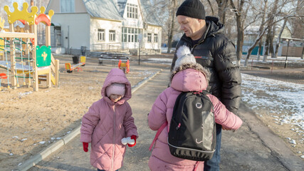 Grandfather walks with his granddaughters after school in the park in sunny winter day