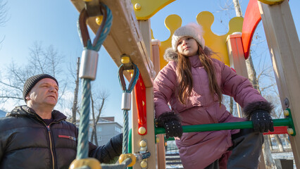 Grandfather with grandchildren playing on the playground on a cold winter day