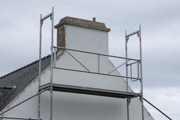 Un échafaudage en métal couvre toute la façade d’une maison en plein ravalement de peinture.