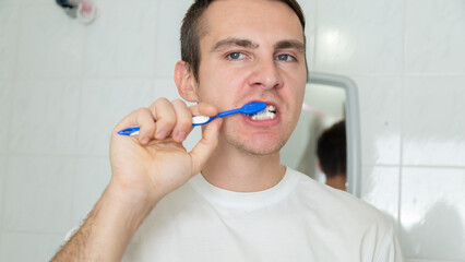 Young man brushing teeth with toothbrush at home in the bathroom