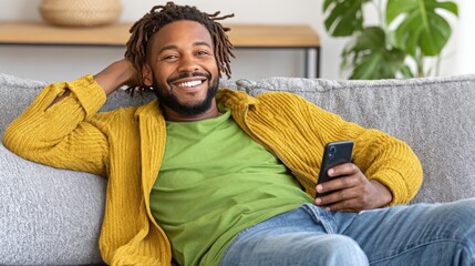 Happy man with dreadlocks relaxing on sofa while using smartphone in a cozy living room