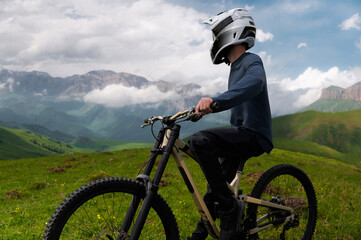 Rider cyclist man wearing mask and full face helmet standing on his bike on top of hill high in mountains. Space copy background for mountain biking