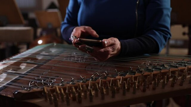 close-up shows a woman's hands playing an ornate wooden zither with plectrums. A microphone captures the beautiful sound of this traditional Middle Eastern folk instrument.