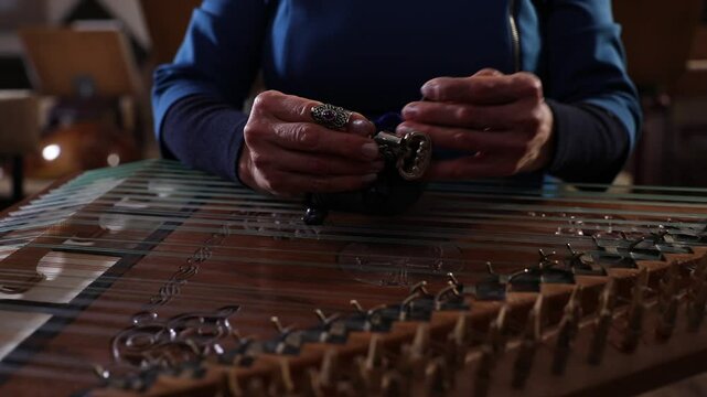 close-up shows a woman's hands playing an ornate wooden zither with plectrums. A microphone captures the beautiful sound of this traditional Middle Eastern folk instrument.