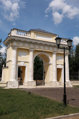 Fototapeta premium Captivating image of an elegant historic archway, framed by a vintage lamp post under a partly cloudy sky. Stunning architectural details and lush landscape provide a timeless charm.