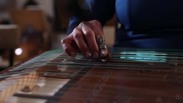 close-up shows a woman's hands playing an ornate wooden zither with plectrums. A microphone captures the beautiful sound of this traditional Middle Eastern folk instrument.