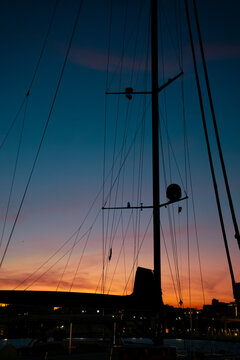 Sailboat silhouettes against a vibrant sunset in a coastal marina during twilight hours