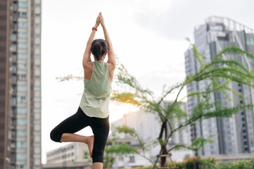Asian woman in 30s fitness yoga workout. Stretching exercise reduces medical injury risk shoulder pain muscle strain inflammation. Healthy lifestyle wellness healthcare in urban city at sunset