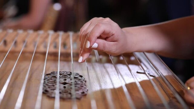 close-up shows a woman's hands playing an ornate wooden zither with plectrums. A microphone captures the beautiful sound of this traditional Middle Eastern folk instrument.