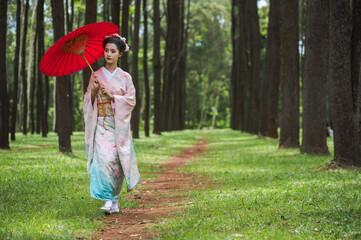 Pretty young Japanese Geisha or Maiko dressing in traditional kimono or yukata costume holding red...