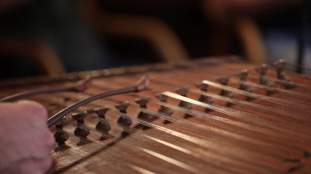 close-up shows a woman's hands playing an ornate wooden zither with plectrums. A microphone captures the beautiful sound of this traditional Middle Eastern folk instrument.
