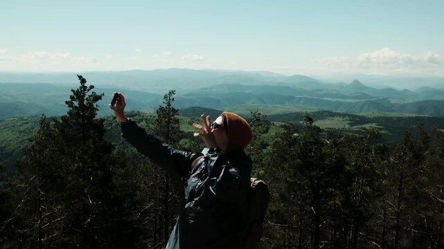Female traveler taking selfie with breathtaking spring landscape in the background, standing confidently above the forest in Zlatibor, Serbia country. Travel blogger making video outdoor
