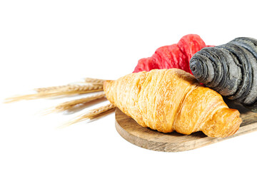 Red, black and classic croissants and ears of wheat on a wooden board.