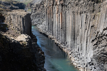 Towering basalt columns rise dramatically alongside the crystal-clear waters of the river in...