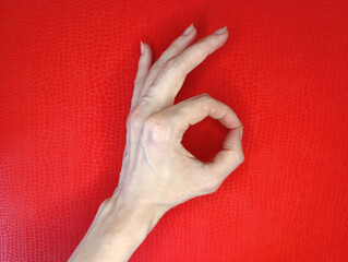Hand gesture forming an okay sign against a vibrant red background captures a positive expression...