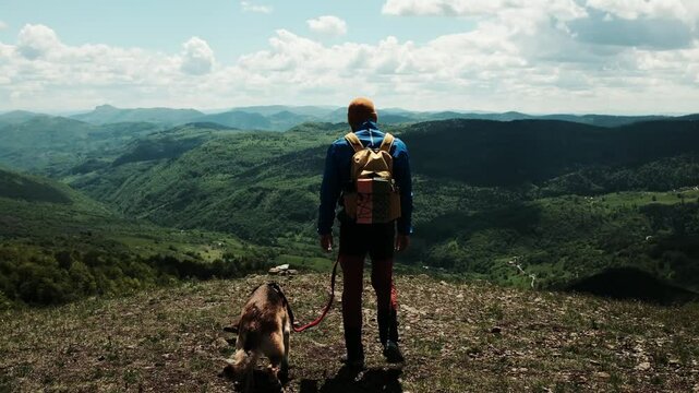 Man with backpack with arms open beside his dog on Mount Cigota, enjoying freedom and fresh mountain air. Traveler walking with German shepherd. Rear view. Travel with pet concept