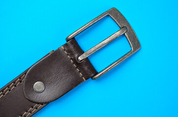 Close-up of brown leather belt with metal buckle on blue background