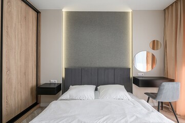 Cozy bedroom with a grey headboard, white linens, floating nightstands, two round mirrors, and a...