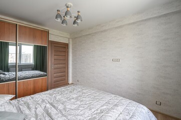 cozy bedroom with a bed, wardrobe with mirrors, and a modern chandelier