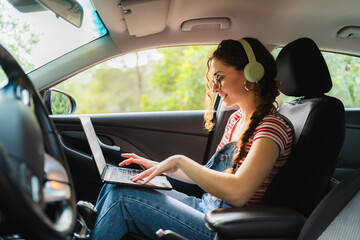 Freelancer working remotely from her car using laptop and headphones