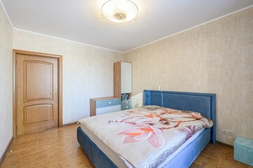 Cozy bedroom featuring a blue bed with floral bedding, a wooden door, and beige textured walls. A...