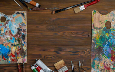 Old used brushes and palette knife in an artist's studio, palette with multi-colored spots of oil or acrylic paint, paint tubes. Copy space