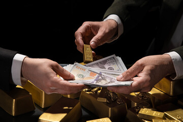 A hand giving a gold bar to another person holding a wad of dollar bills. Gold Nuggets. Bank gold bars. Gold reserv holdings concept. Savings and investments, business and finance