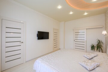 Bright bedroom with a bed, mounted TV, and paneled doors. A decorative ceiling and minimalist style add to the room's appeal