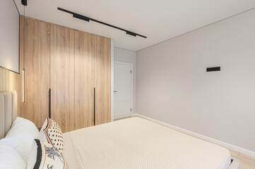 modern bedroom featuring a bed with decorative pillows, a wood-paneled headboard and wardrobe, and...
