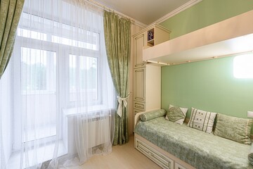 bright bedroom with green walls, sheer white curtains, and patterned green drapes. A bed sits...
