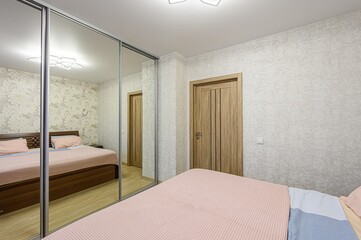 modern bedroom featuring a mirrored closet, a wooden bed with pink and blue bedding, and patterned...