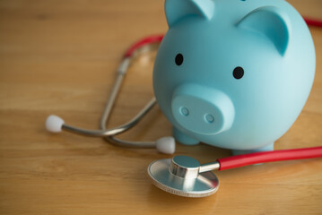 Blue piggy bank and red stethoscope on wooden table background copy space. Money savings for medical, healthcare, life insurance or personal financial checkup and so on concept.