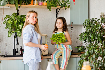 Young woman and her daughter making healthy green smoothie on home kitchen.