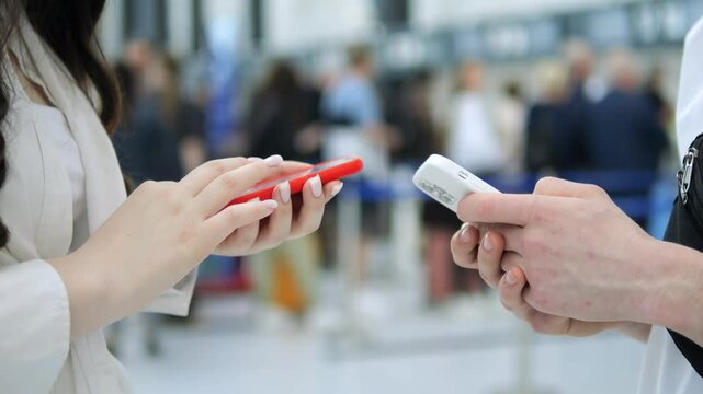 Woman is holding a red phone and a white card. She is talking to someone else. The scene is crowded with people