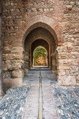 Sequence of Moorish arches in the Alcazaba of Málaga, with intricate stone and brickwork framing a view into a lush courtyard.