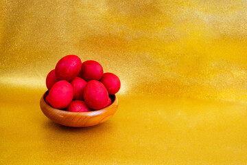Red boiled easter eggs pile in a wooden bowl on golden glitter background with copy space