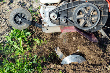 Garden tiller for cultivating field, loosens soil. Handheld motor plow throwing dirt with motion...
