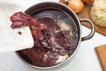 Pouring chicken liver in a water filled pot for washing before cooking, soft focus close up