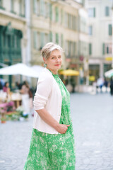 Outdoor portrait of beautiful 55 -60 year old woman posing with city background, fashion and helthy lifestyle