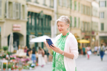 Outdoor portrait of beautiful 55 -60 year old woman posing with city background, holding phone