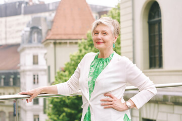 Outdoor portrait of beautiful 55 -60 year old woman posing with city background, fashion and helthy lifestyle