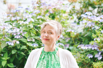 Outdoor closeup portrait of beautiful mature woman of 55 - 60 year old, nice short haircut with grey hair, posing with flowers background, lifestyle and fashion