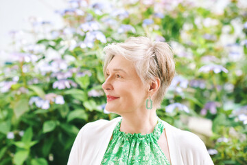 Outdoor closeup portrait of beautiful mature woman of 55 - 60 year old, nice short haircut with grey hair, posing with flowers background, lifestyle and fashion