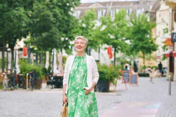 Outdoor portrait of beautiful 55 -60 year old woman posing with city background, fashion and helthy lifestyle
