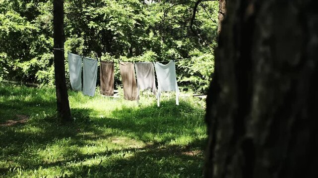 Laundry drying on a clothesline in the forest, with sunlight filtering through the trees on a peaceful spring day in Serbian village. Horizontal 4k footage