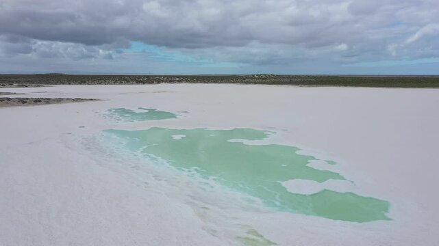 Turquoise water and salt flat surface, reflecting cloudy sky and revealing environmental transformation under expansive landscape. Saline pond in Guerrero Negro, Baja California, Mexico