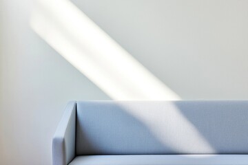 Minimalist light blue sofa against a light gray wall with a soft diagonal beam of sunlight creating a calm, airy atmosphere.