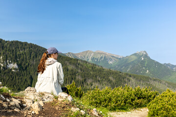 girl tourist sits on the edge of a cliff enjoying the view of the mountains and valley. travel and hiking in the mountains, Tatra Mountains, Poland