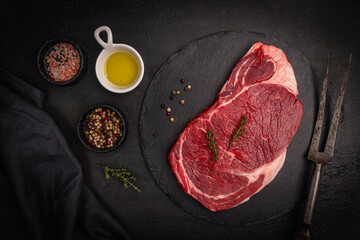 Raw fresh beef steak with spices on a dark slate, stone or concrete background. Top view with copy...